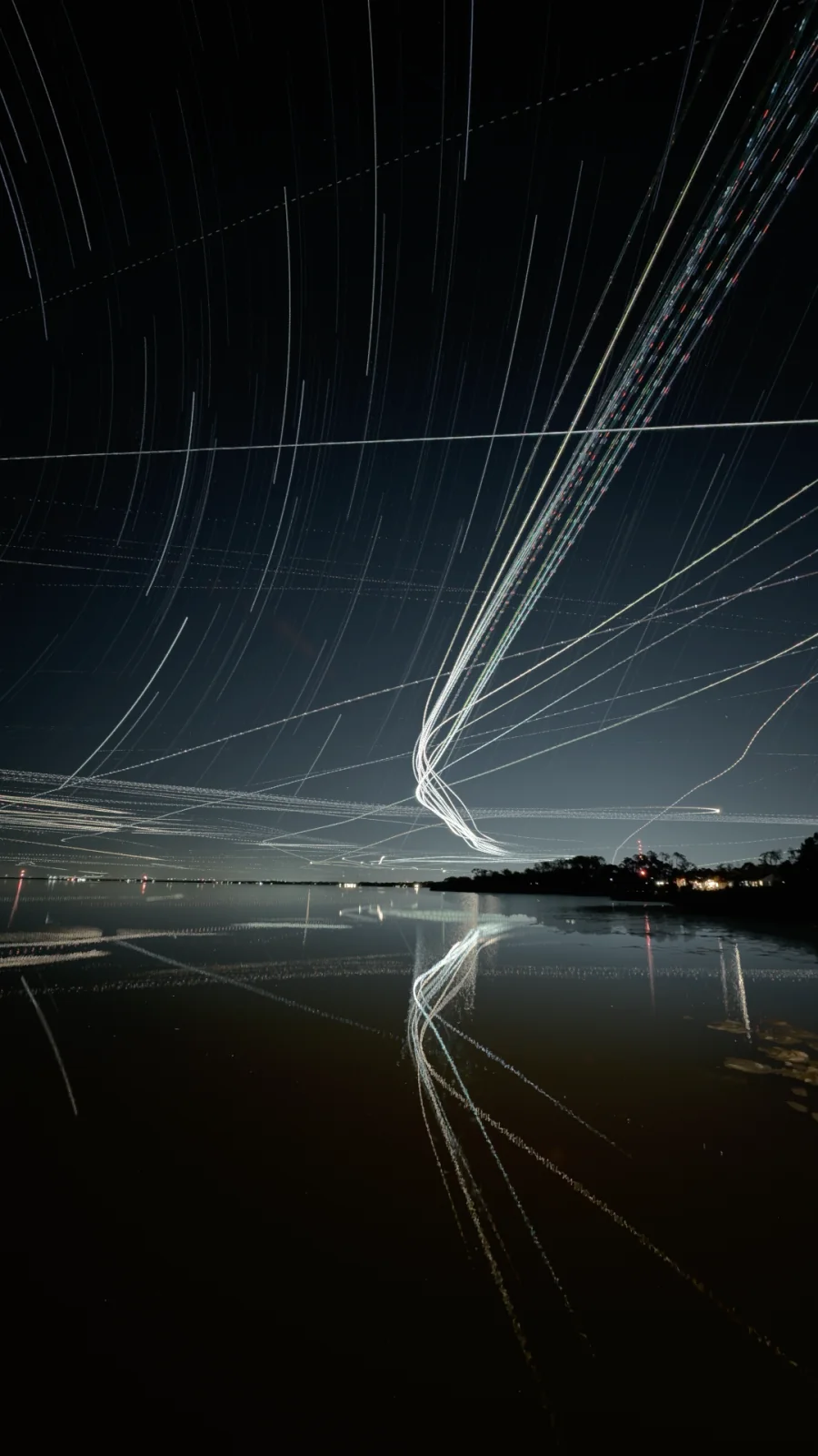 Aircraft and star trails reflected over water